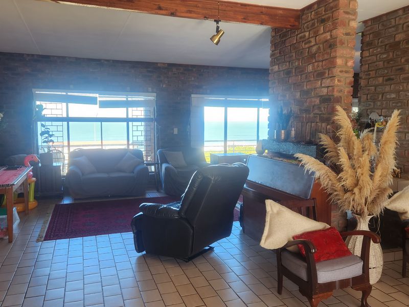 Spacious living room featuring exposed brick walls, a timber ceiling beam, tiled flooring, and a built-in fireplace with expansive ocean views.