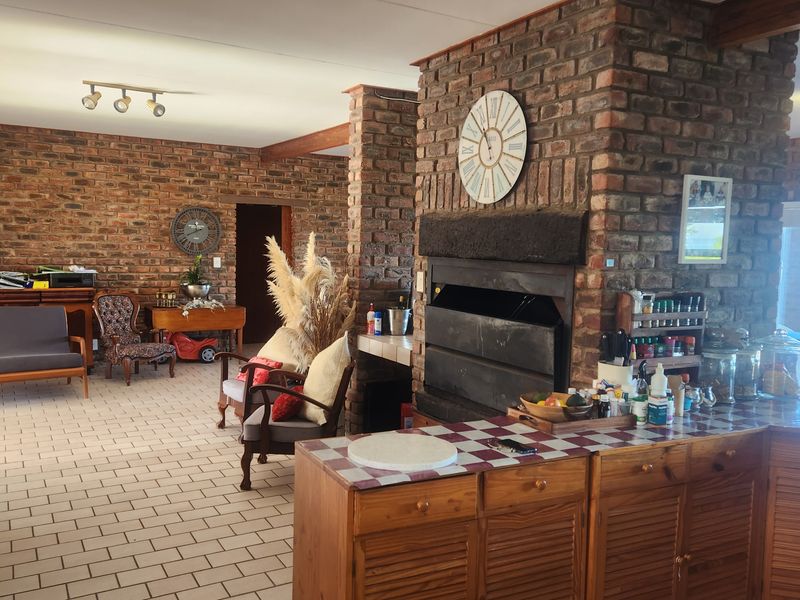 Spacious open-plan living area featuring exposed brick walls, a central built-in fireplace, and tiled flooring with integrated kitchen cabinetry.