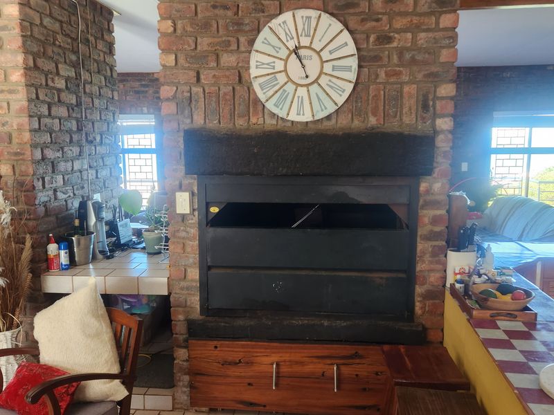 Open plan living area featuring a prominent exposed brick fireplace with built-in braai and tiled kitchen counter space.
