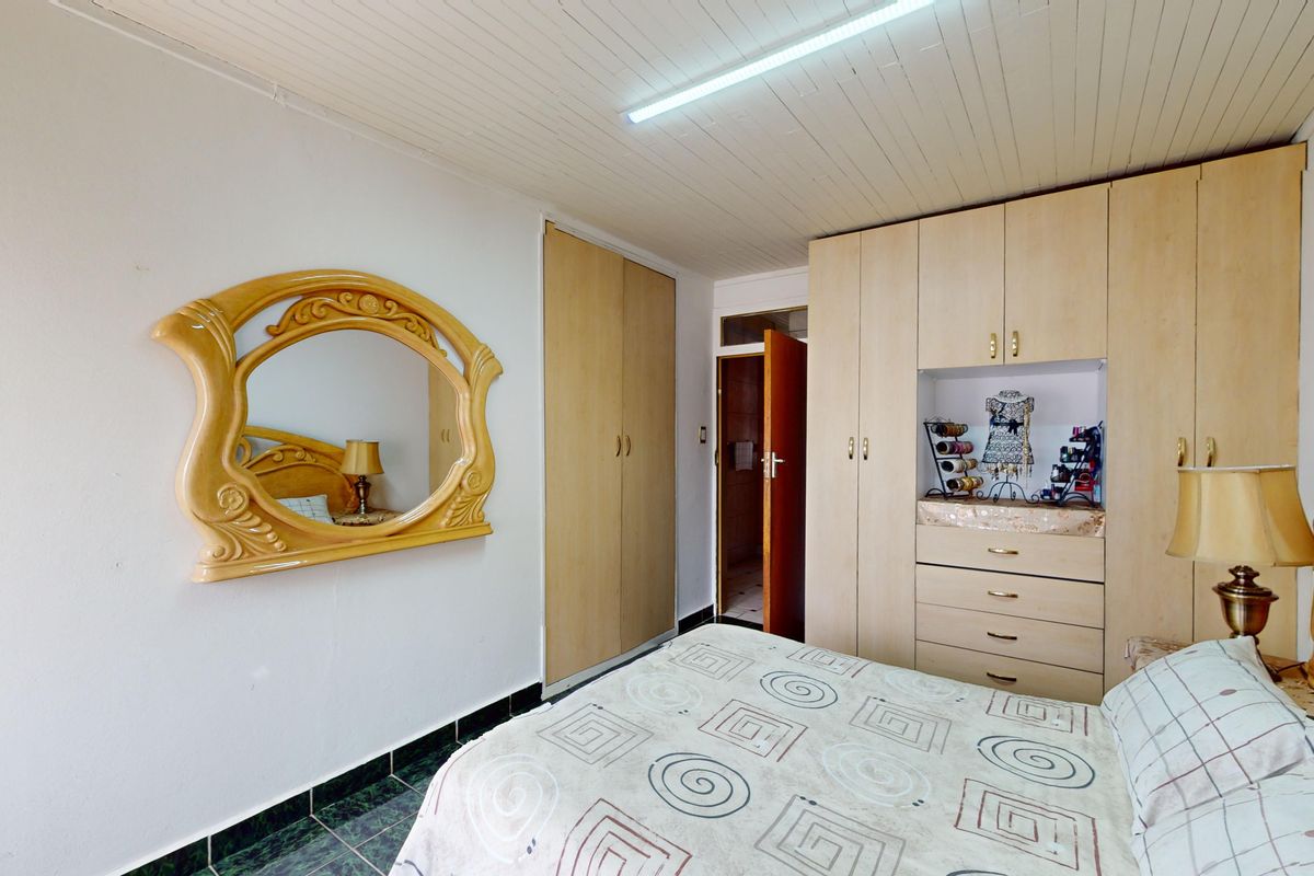 A bedroom featuring built-in wooden cupboards, tiled flooring, and a tongue and groove ceiling, offering functional storage and a neutral layout.