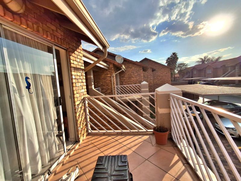 A private balcony featuring tiled flooring and a metal balustrade, accessible via a sliding glass door, overlooking the complex parking area.