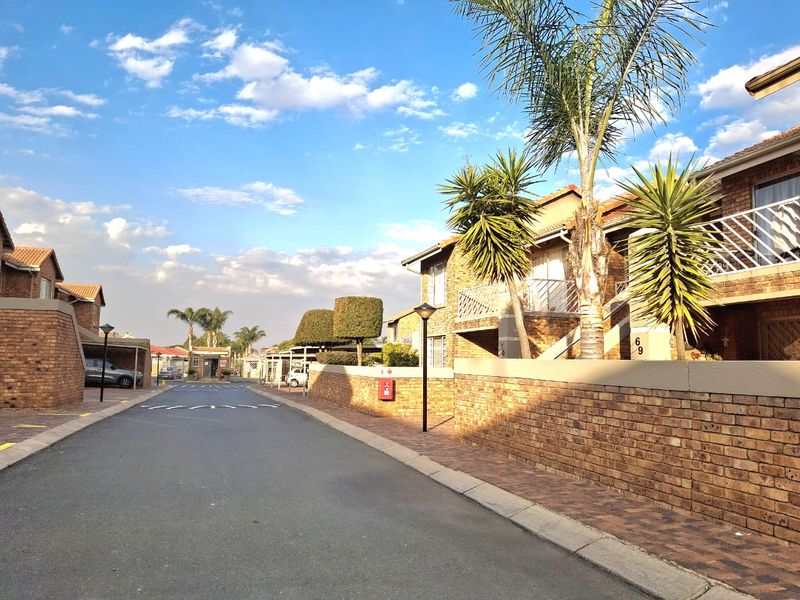 A view of the townhouse complex street, featuring brick facade buildings, paved walkways, and established landscaping.