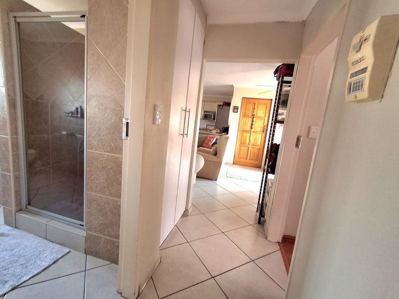 A tiled hallway providing access to a bathroom with a shower enclosure and built-in storage cupboards, leading through to the main living area.