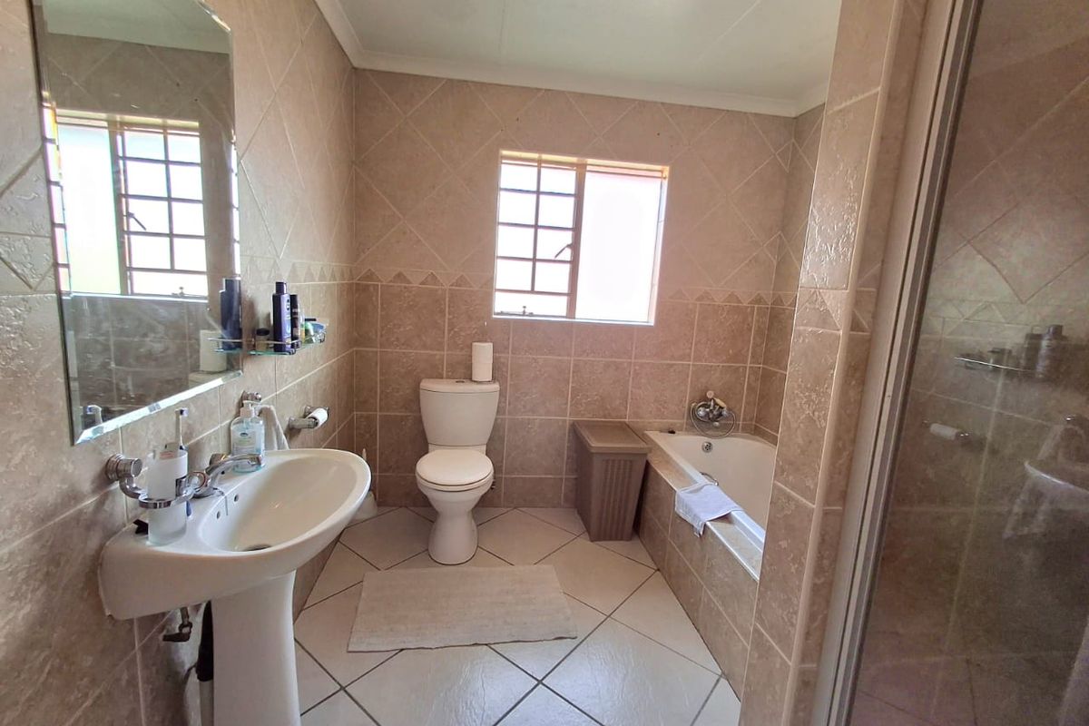 A functional bathroom featuring a pedestal basin, toilet, built-in bathtub, and a separate shower enclosure with neutral wall and floor tiling.