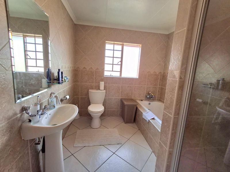 A functional bathroom featuring a pedestal basin, toilet, built-in bathtub, and a separate shower enclosure with neutral wall and floor tiling.