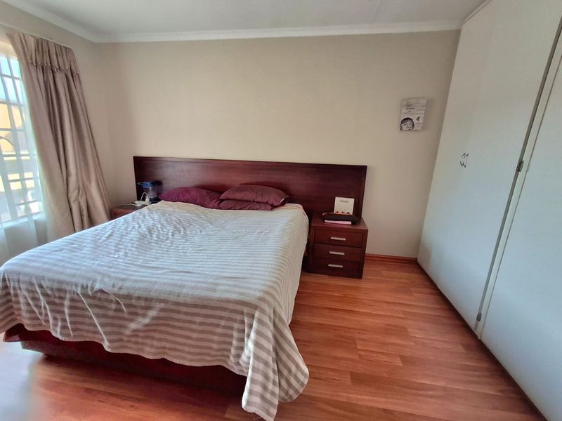 A bedroom featuring laminate flooring, built-in cupboards, and a window with curtaining.