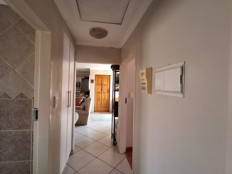A functional hallway featuring tiled flooring, built-in storage cupboards, and access to the home's electrical distribution board and alarm system.