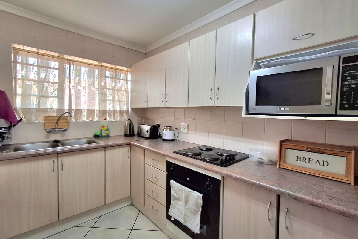 Functional kitchen featuring light-toned laminate cabinetry, stone-look countertops, built-in oven, electric hob, and a double basin sink with tiled backsplash.