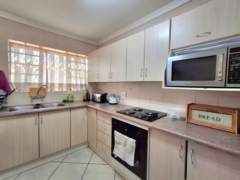 Functional kitchen featuring light-toned laminate cabinetry, stone-look countertops, built-in oven, electric hob, and a double basin sink with tiled backsplash.