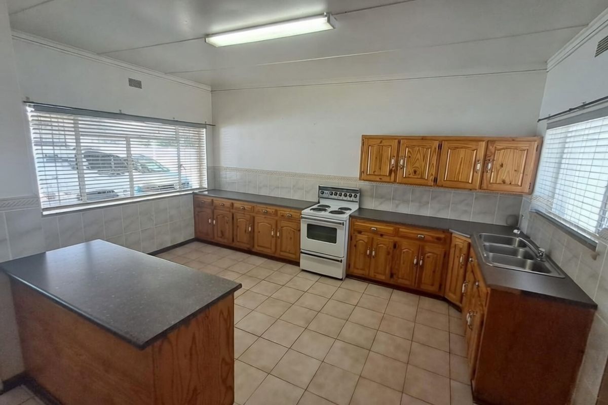 A functional kitchen featuring wooden cabinetry, laminate countertops, a freestanding electric stove, and tiled flooring, offering a classic layout ready for modernization.