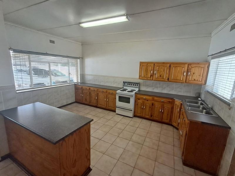 A functional kitchen featuring wooden cabinetry, laminate countertops, a freestanding electric stove, and tiled flooring, offering a classic layout ready for modernization.