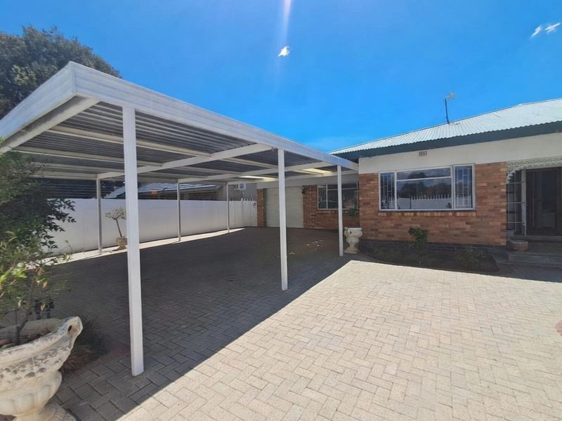 Front exterior view of the property featuring a spacious paved driveway and a large covered carport attached to the main brick building.