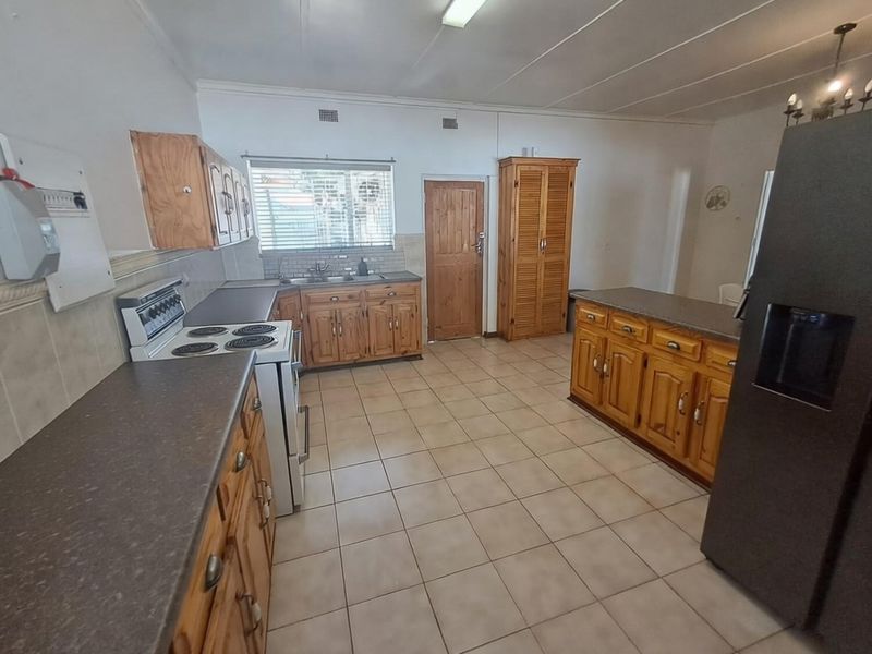 A functional kitchen featuring wooden cabinetry, laminate countertops, tiled flooring, and a freestanding stove, offering a classic layout with ample storage space.