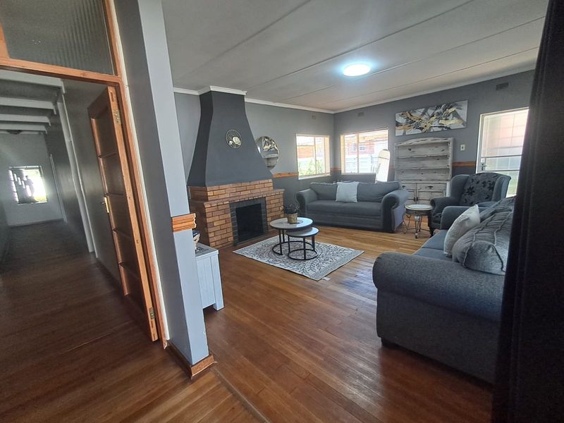 Spacious living room featuring a prominent brick fireplace, hardwood flooring, and classic timber door frames, offering a comfortable and traditional living space.