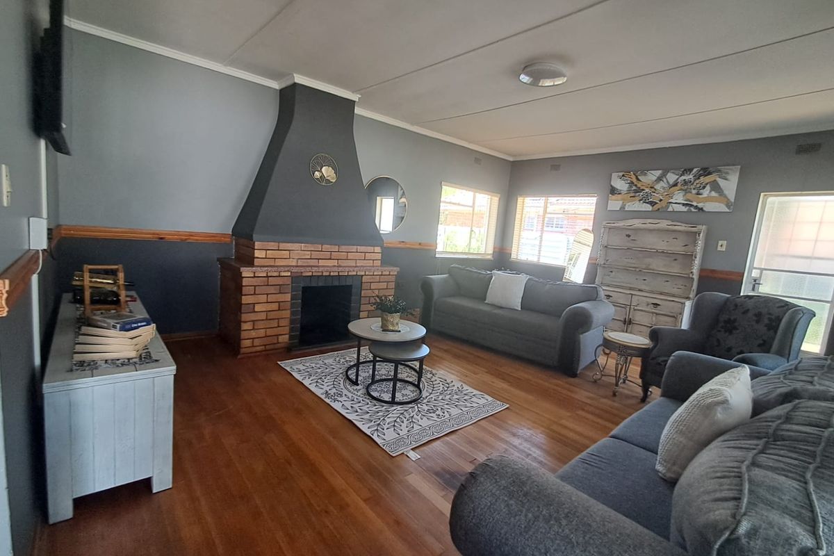 Spacious living room featuring a prominent brick fireplace, hardwood flooring, and a decorative timber dado rail, offering a cozy and traditional atmosphere.