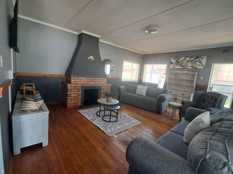Spacious living room featuring a prominent brick fireplace, hardwood flooring, and a decorative timber dado rail, offering a cozy and traditional atmosphere.