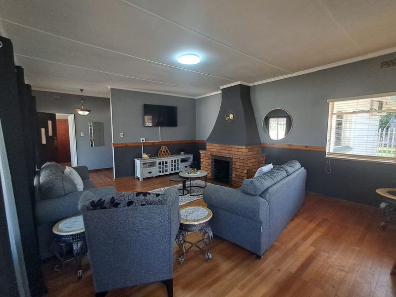 Spacious living room featuring hardwood flooring and a prominent brick fireplace, offering a comfortable and functional layout for relaxation.