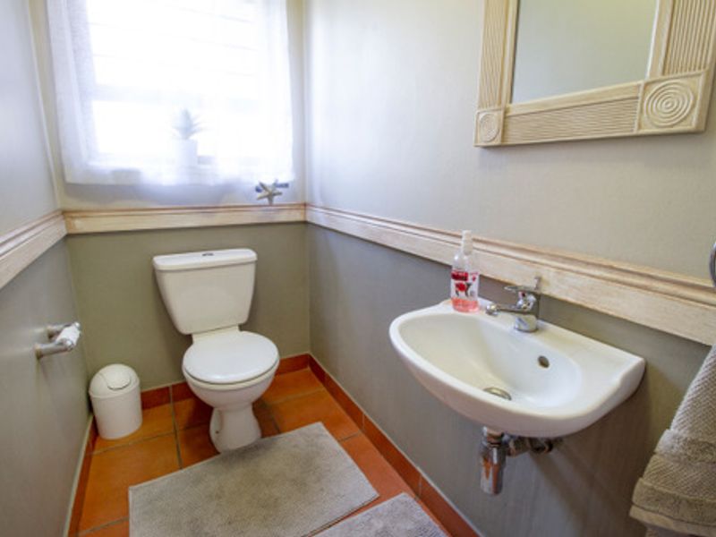 A compact guest bathroom featuring a wall-mounted basin, toilet, and neutral wall finishes with decorative chair rail molding.