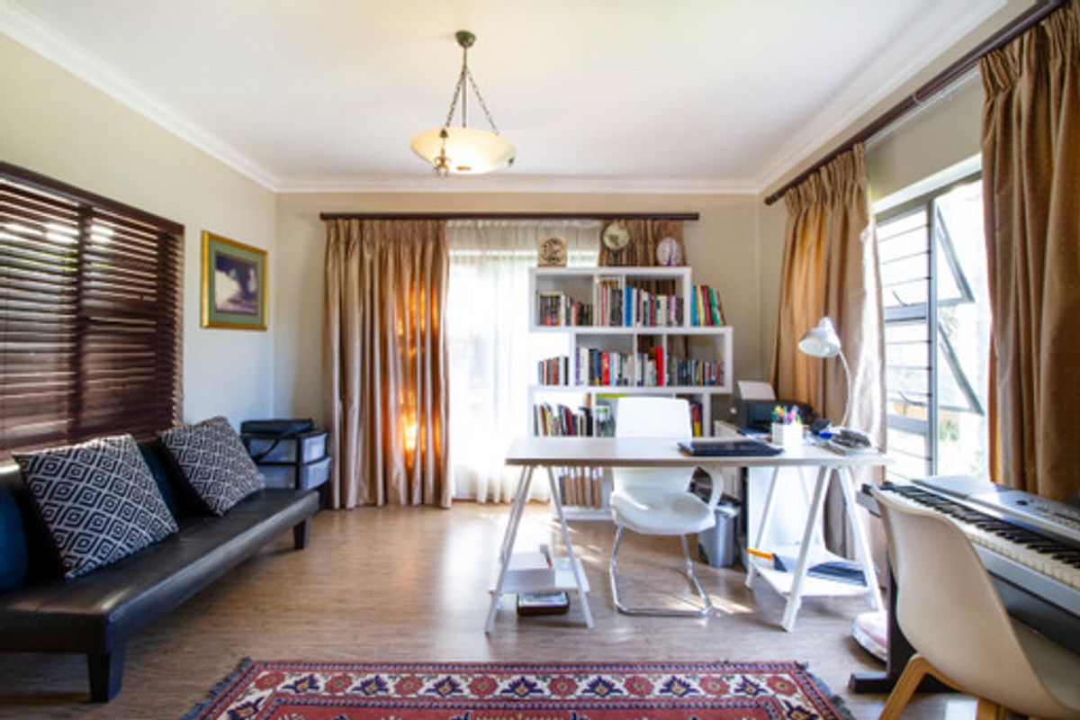 A multi-purpose room currently utilized as a home office and study, featuring laminate flooring, cove cornicing, and large windows allowing for natural light.