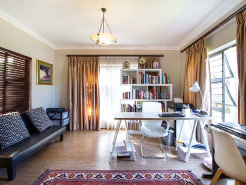 A multi-purpose room currently utilized as a home office and study, featuring laminate flooring, cove cornicing, and large windows allowing for natural light.