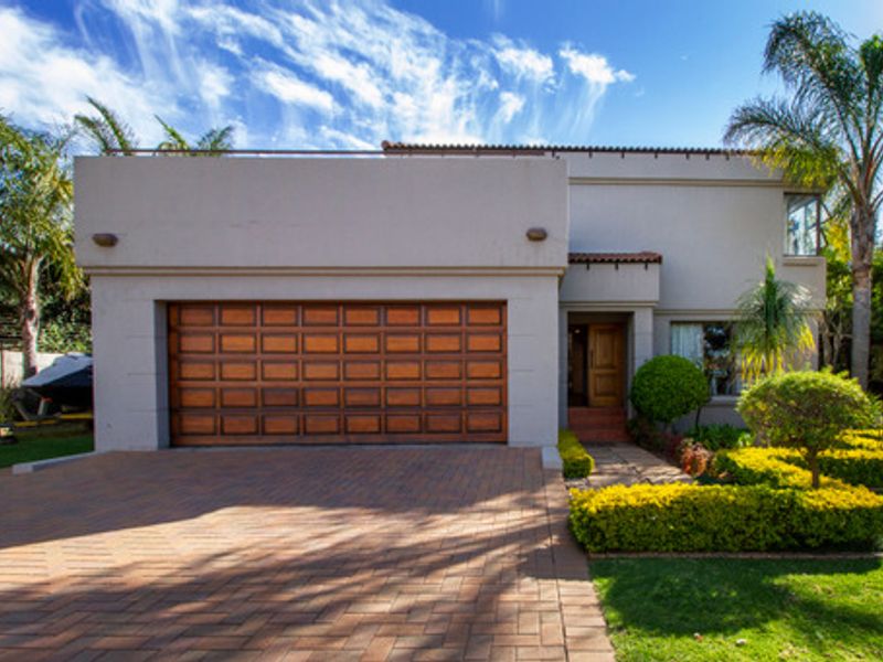 Front elevation of a modern house featuring a paved driveway, a prominent wooden sectional garage door, and a well-maintained landscaped garden.