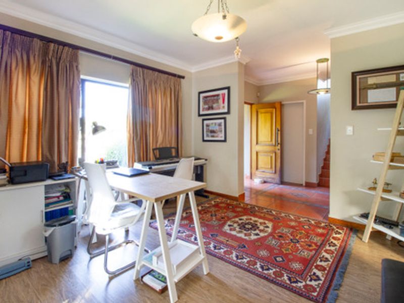 A functional home office space featuring laminate flooring, cove cornicing, and a solid timber door leading to the hallway.