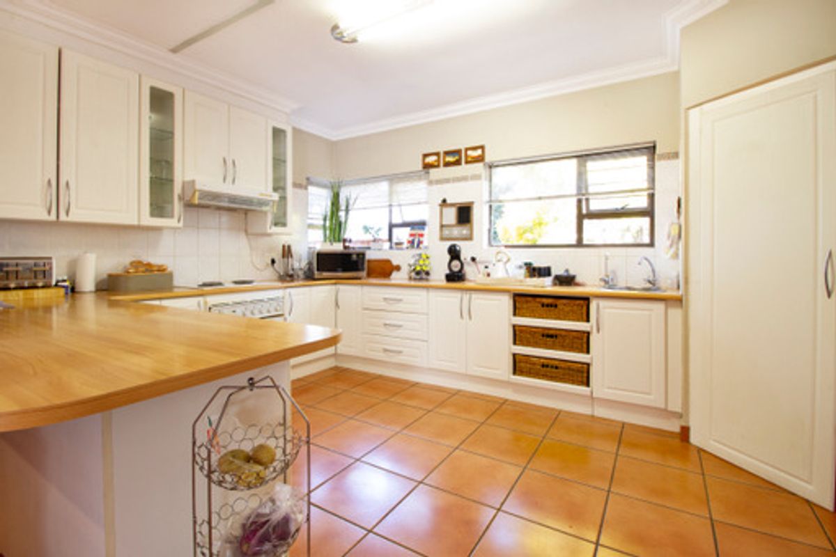 A functional kitchen featuring white cabinetry, wooden countertops, tiled flooring, and ample natural light from the windows.