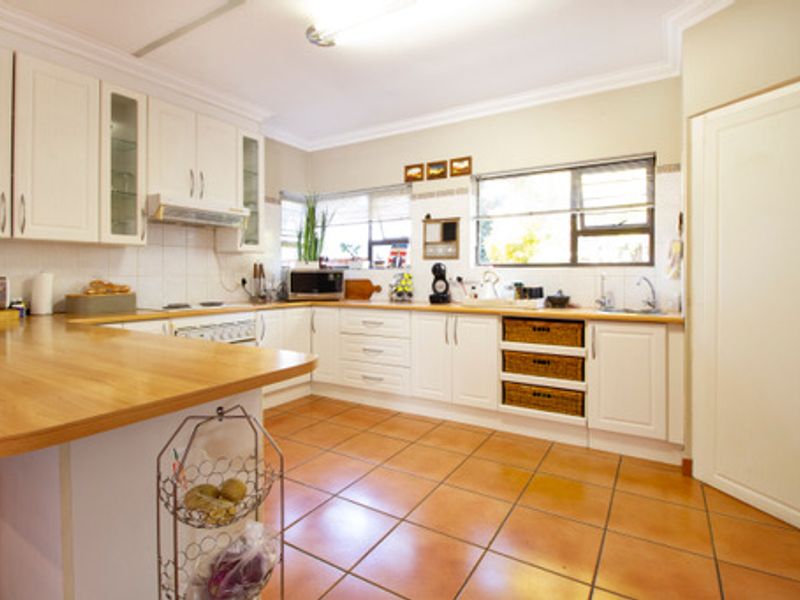 A functional kitchen featuring white cabinetry, wooden countertops, tiled flooring, and ample natural light from the windows.