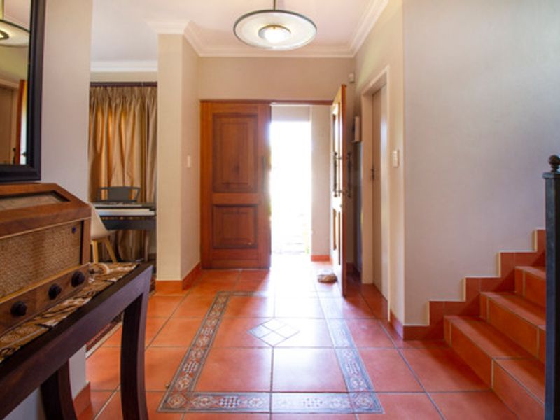 Welcoming entrance hall featuring terracotta floor tiles with decorative inlay, a solid wooden front door, and a staircase with a metal railing.