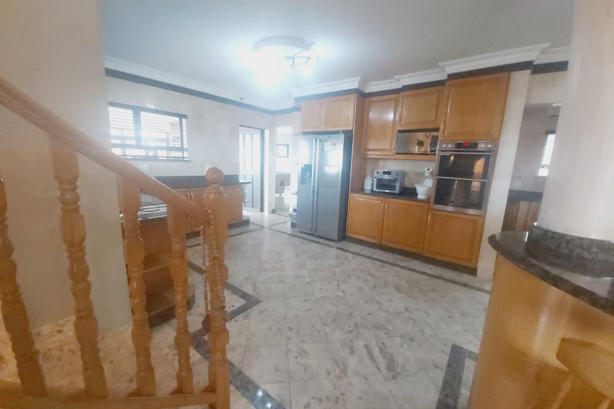 Spacious kitchen featuring wooden cabinetry, built-in double oven, stone countertops, and tiled flooring, with an adjacent staircase.