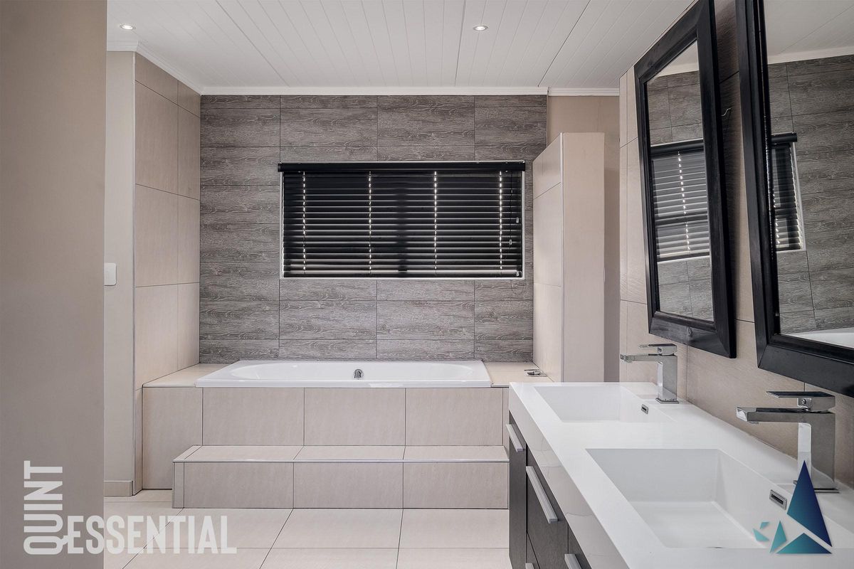 Modern bathroom featuring a built-in bathtub with tiled surround, dual vanity with integrated sinks, and contemporary wall tiling.