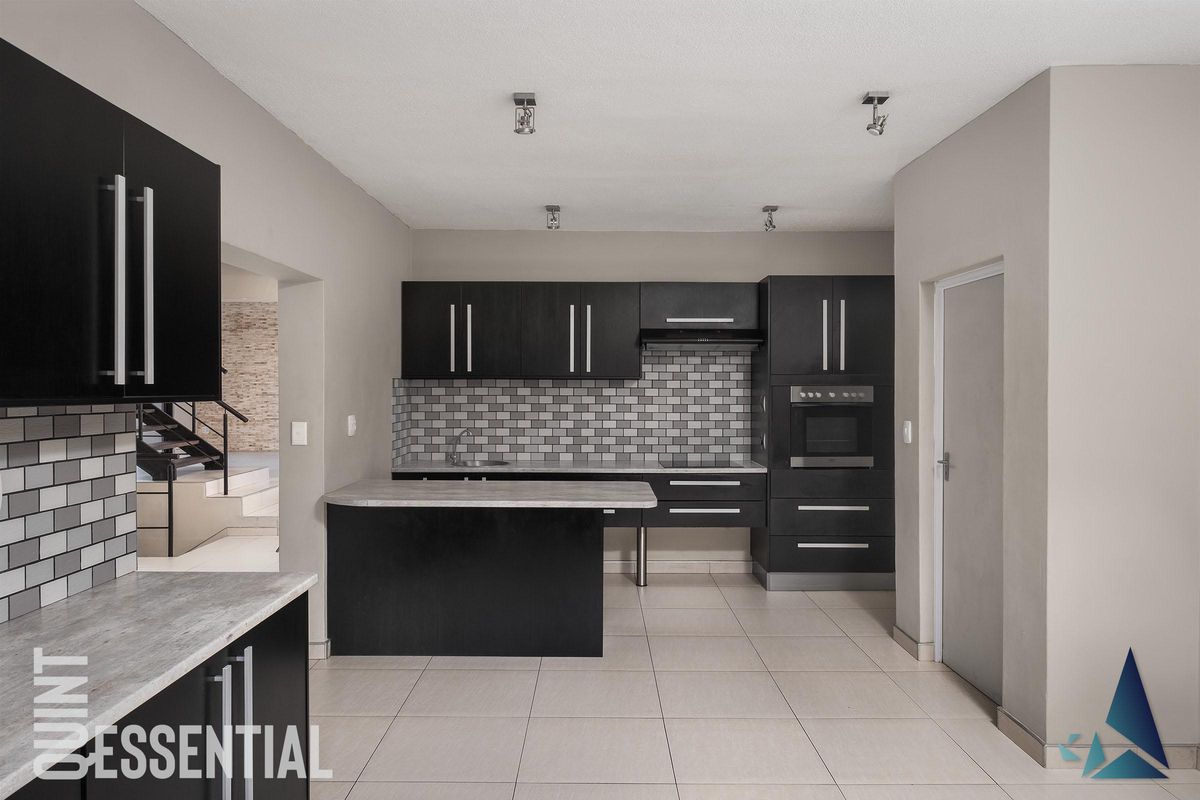 Modern kitchen featuring dark cabinetry, stone-look countertops, a subway tile backsplash, and built-in oven, with tiled flooring throughout.