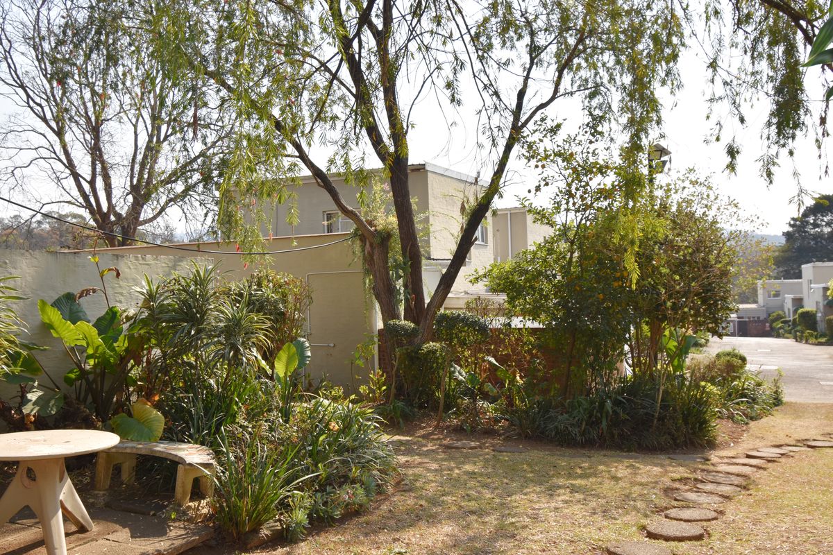 A view of the rear garden area featuring established trees, landscaped garden beds, and a paved pathway leading towards the townhouse exterior.