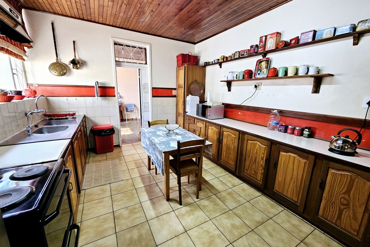A functional kitchen featuring wooden cabinetry, tiled flooring, a double basin sink, and a classic wooden ceiling, offering a traditional aesthetic.