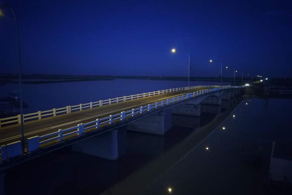 An aerial night view of a bridge spanning over a body of water, illuminated by street lights.