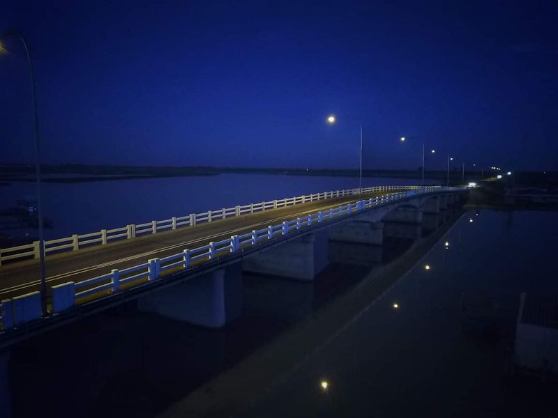 An aerial night view of a bridge spanning over a body of water, illuminated by street lights.