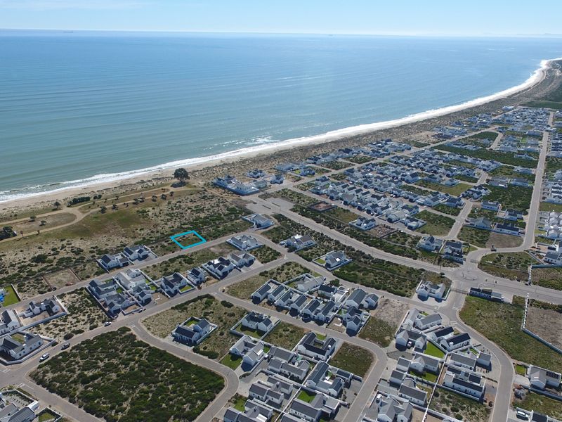 Aerial view of a vacant residential plot situated in a coastal development, highlighting its proximity to the beach and surrounding neighborhood infrastructure.