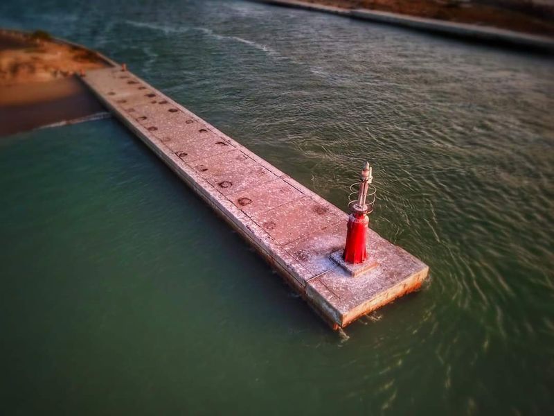 Aerial view of a concrete pier extending into the water, featuring a red navigation beacon at the end.