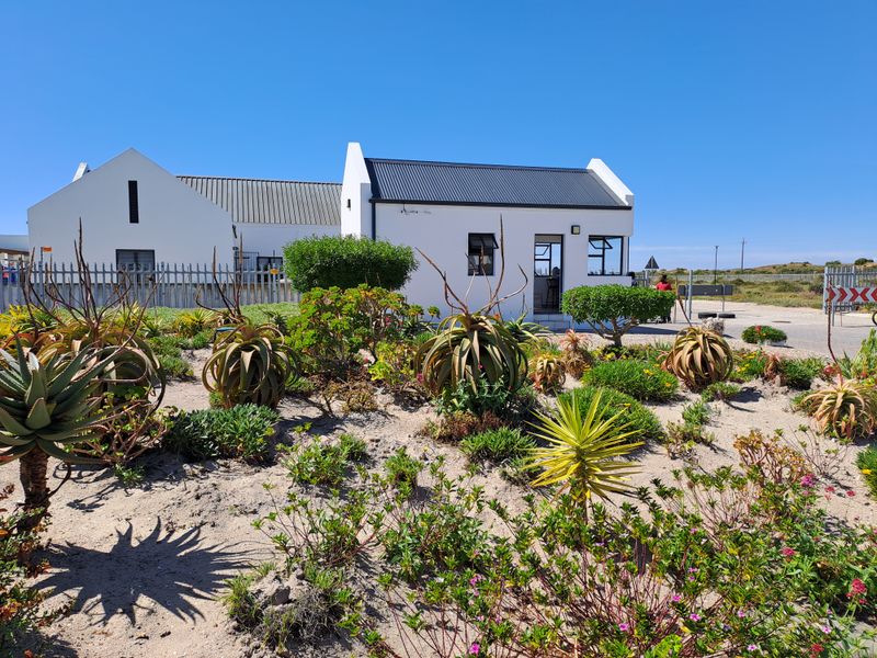 A well-maintained residential property featuring a white facade, corrugated metal roof, and a landscaped garden with native plants and security fencing.