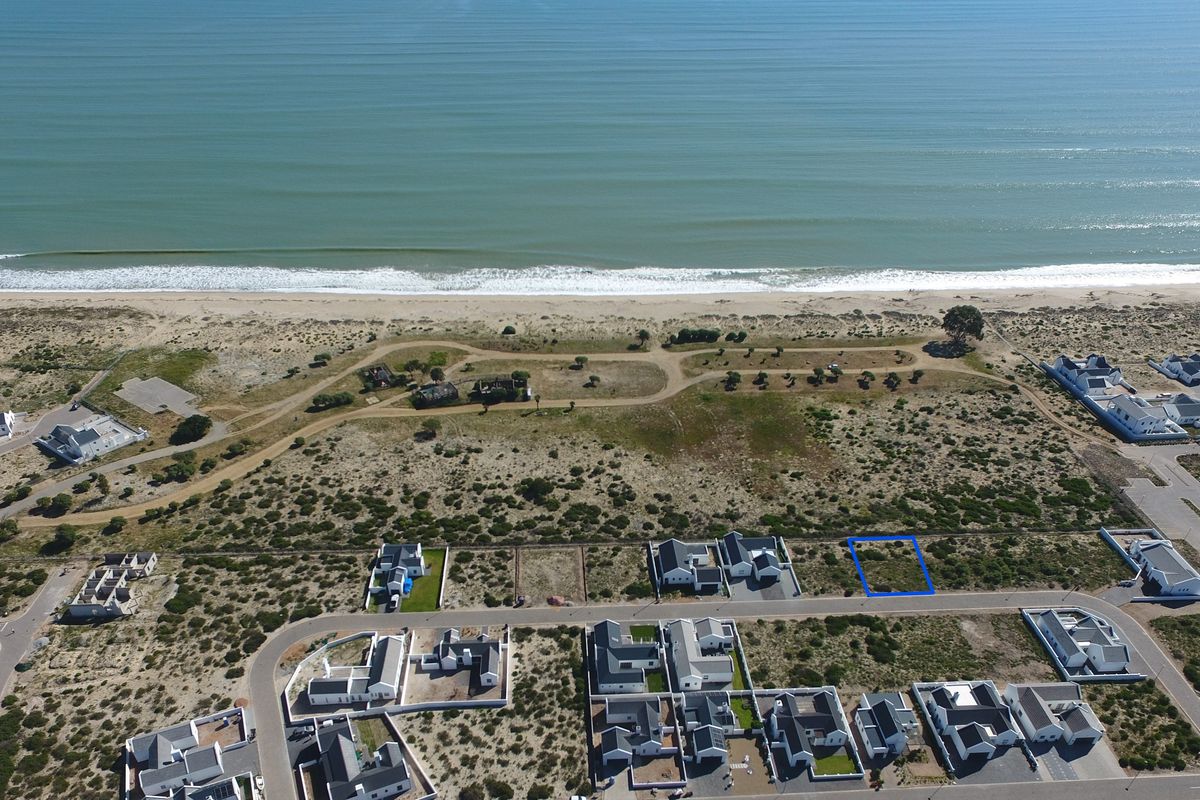 Aerial view of a vacant residential plot situated in a coastal estate, offering proximity to the beach and surrounding residential development.