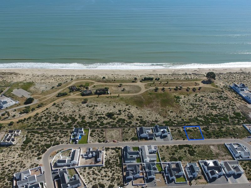 Aerial view of a vacant residential plot situated in a coastal estate, offering proximity to the beach and surrounding residential development.