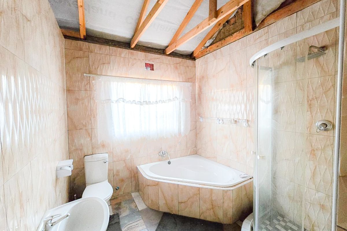 Bathroom featuring a corner bathtub, glass shower, and pedestal basin, with exposed timber roof trusses and unfinished ceiling requiring completion.
