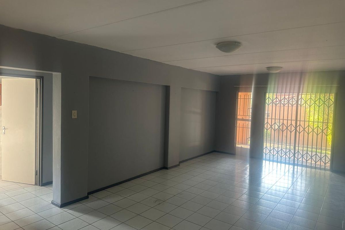 An empty, open-plan living area featuring neutral grey walls, tiled flooring, and a secure metal gate leading to the exterior.