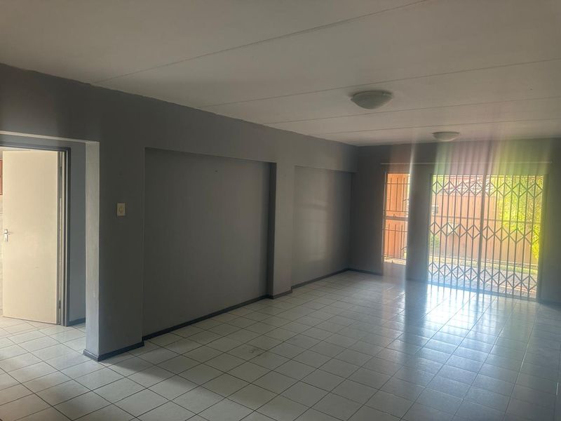 An empty, open-plan living area featuring neutral grey walls, tiled flooring, and a secure metal gate leading to the exterior.