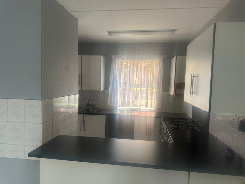 A functional kitchen featuring white built-in cabinetry, dark laminate countertops, a gas hob, and a tiled backsplash with a window providing natural light.