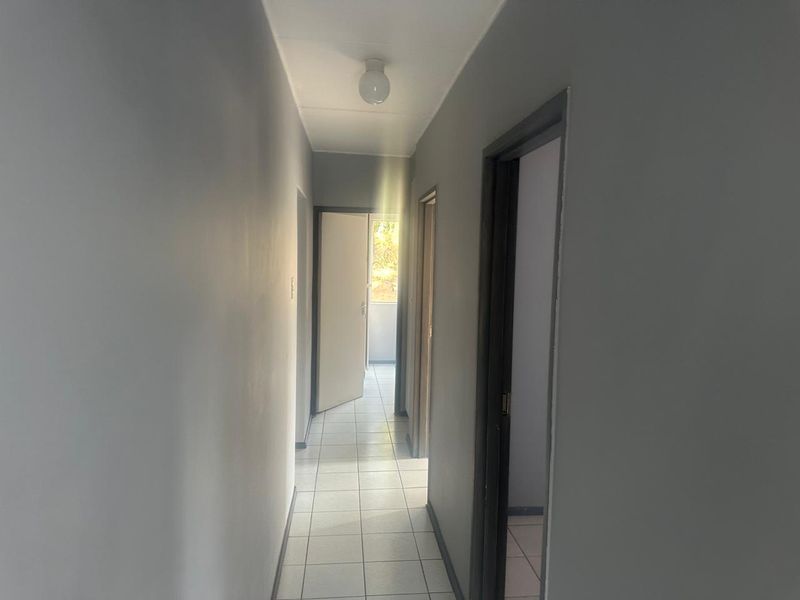 A clean, empty hallway featuring neutral grey walls, tiled flooring, and multiple internal doorways leading to other rooms.