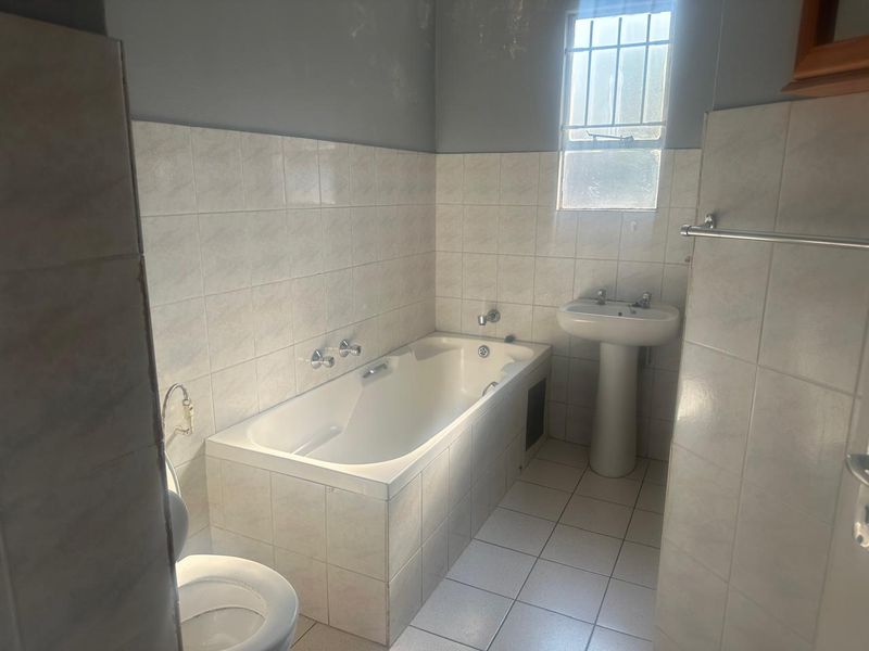A functional bathroom featuring a built-in bathtub, pedestal basin, and tiled finishes, requiring some cosmetic updates to the wall paint and overall presentation.