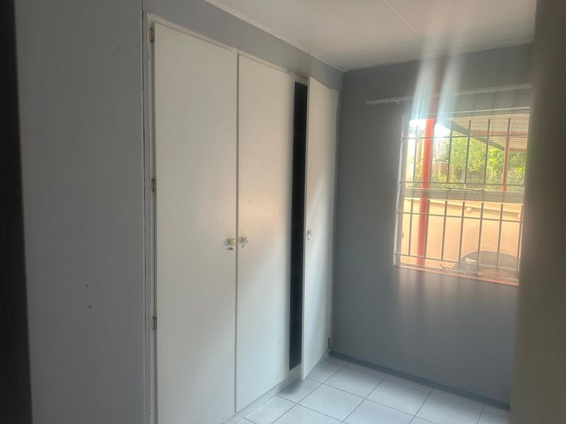 A simple bedroom featuring tiled flooring, built-in cupboards, and a window fitted with security bars.