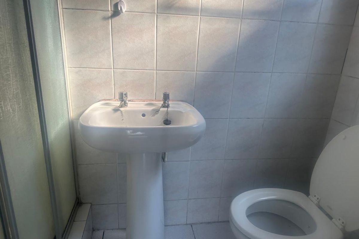 A functional bathroom featuring a pedestal basin, toilet, and shower enclosure with tiled walls and flooring, requiring cosmetic updates to improve its overall condition.
