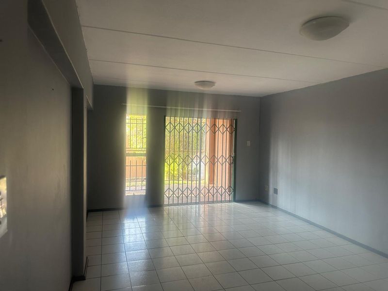 An empty, open-plan living area featuring neutral grey walls, tiled flooring, and a sliding door with a security gate leading to the exterior.
